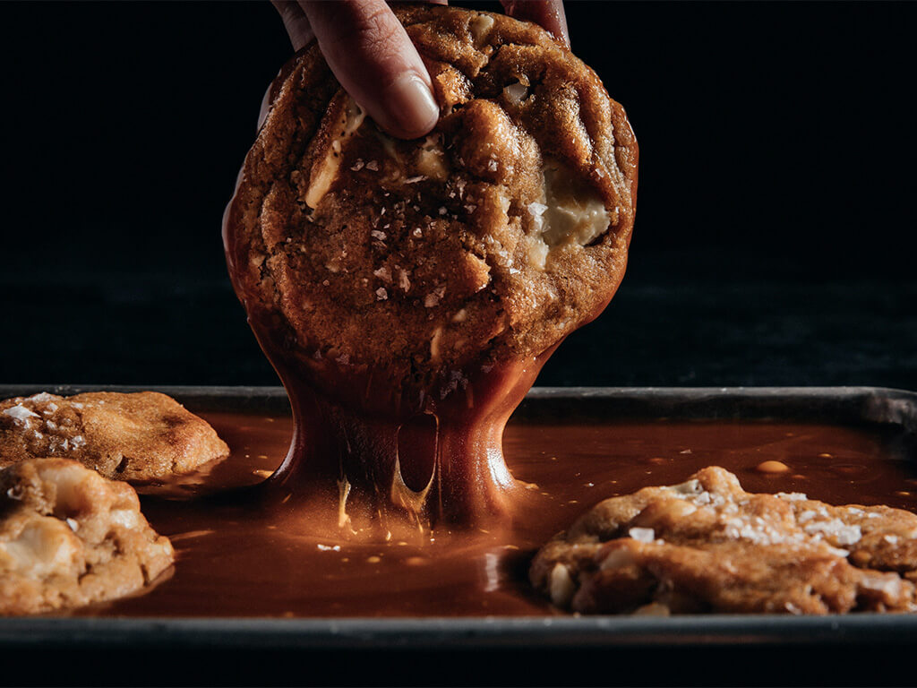 A Crumbl cookie being dipped into a chocolate sauce.