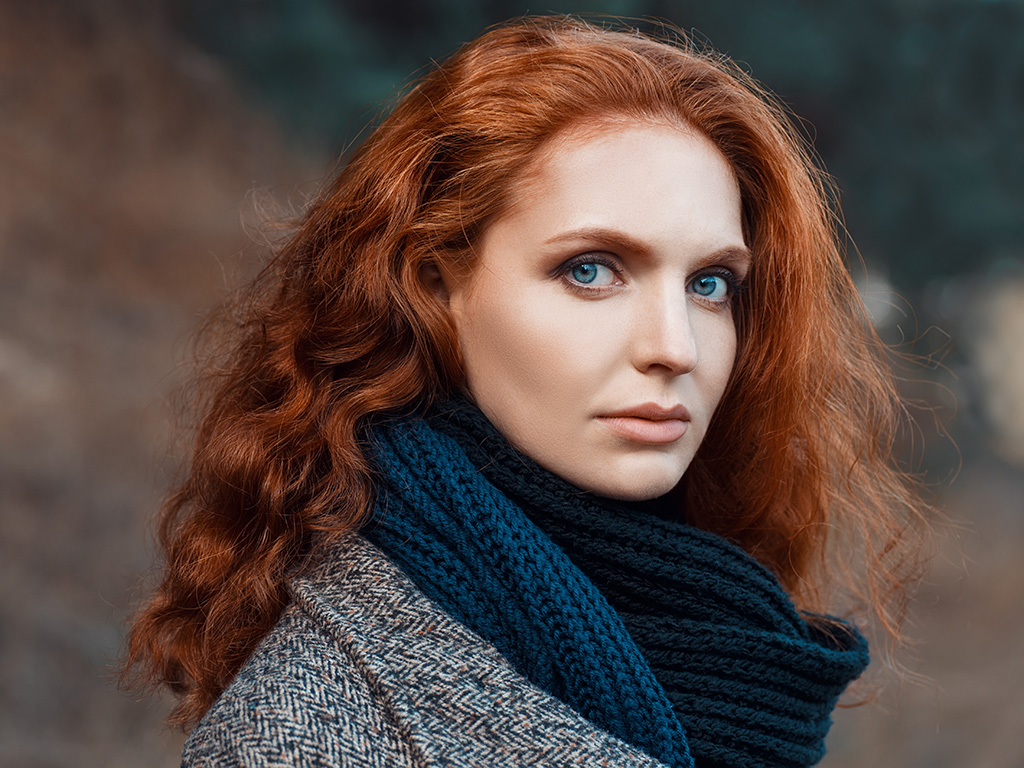 Closeup portrait of beautiful woman with red hair and blue eyes posing outdoors
